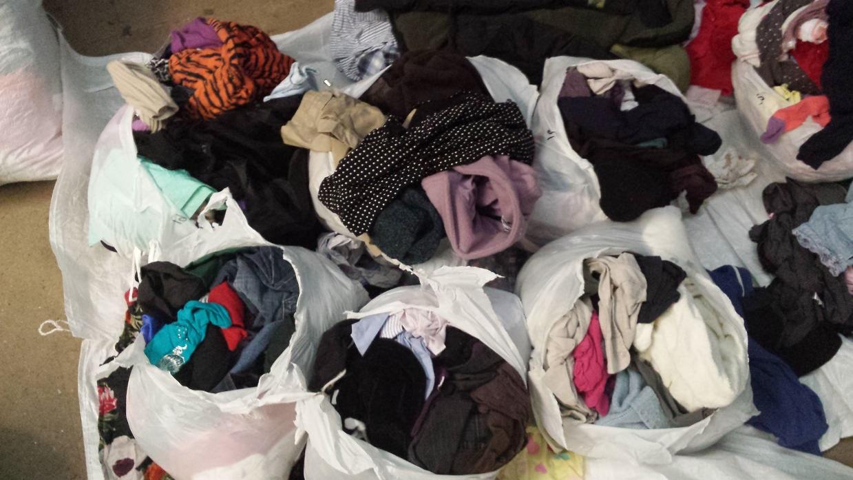 Worki z odzieżą używaną: różnorodna faktura, wzory i kolory. Ubrania w workach foliowych, widoczne fragmenty koszul, bluzek i spodni, zróżnicowana kolorystyka.