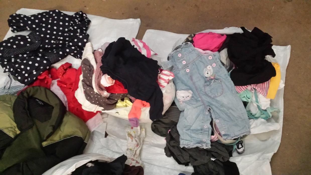 Stos ubrań damskich i dziecięcych na białym worku foliowym: bluzka w grochy, czerwona koszulka, jeansowe ogrodniczki z aplikacją, czarny sweter.