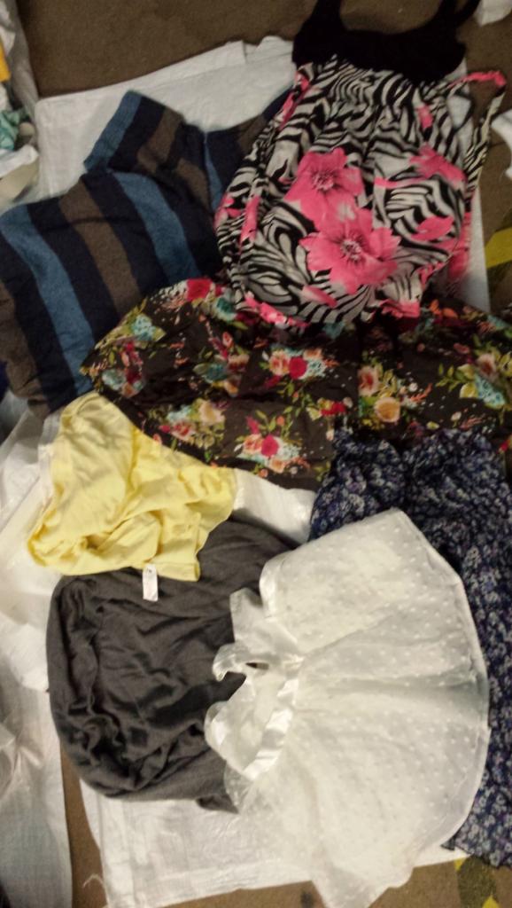 Stos ubrań damskich z różnymi wzorami i kolorami, w tym bluzki w paski, sukienki w kwiaty i topy z nadrukami, ułożonych na białym materiale.