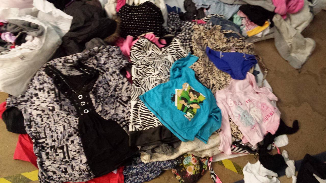 Stos ubrań damskich i dziecięcych w Glasgow: wzorzysta bluzka, bluza z kapturem, spodnie, bielizna, bluzki. Ubrania są posortowane na podłodze.