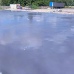 Świeżo wylana, gładka posadzka na zewnątrz, odbijająca niebo. W tle widoczne drzewa, słupy wysokiego napięcia i przyczepa ciężarówki.