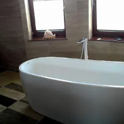 Nowoczesna łazienka z wolnostojącą wanną, płytkami w odcieniach brązu i beżu, oraz oknami z dekoracjami. Uwagę zwraca wzór szachownicy na podłodze.