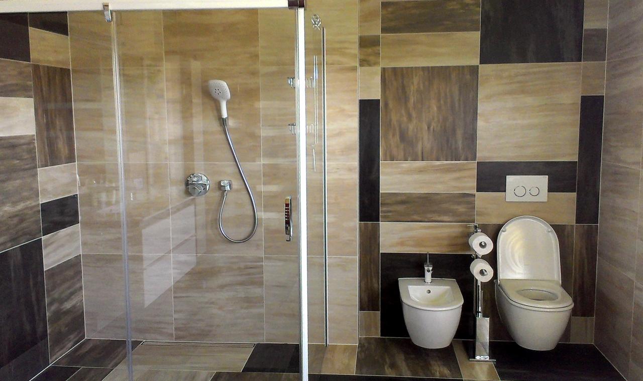 Nowoczesna łazienka z kabiną prysznicową, bidetem i toaletą. Kolorowe płytki na ścianach i podłodze. Chromowana armatura i akcesoria łazienkowe.