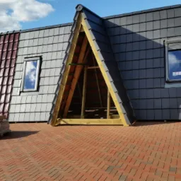 Ekspozycja dachówek w różnych kolorach i fakturach, z oknem dachowym i fragmentem konstrukcji więźby, prezentowana na ceglanej powierzchni.