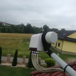 Zewnętrzna antena satelitarna zamontowana na dachu z widocznymi kablami koncentrycznymi i krajobrazem w tle.