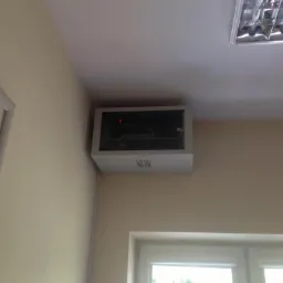 Naścienna szafka serwerowa w biurze, widoczny sprzęt sieciowy i diody sygnalizacyjne, z oknem w tle.