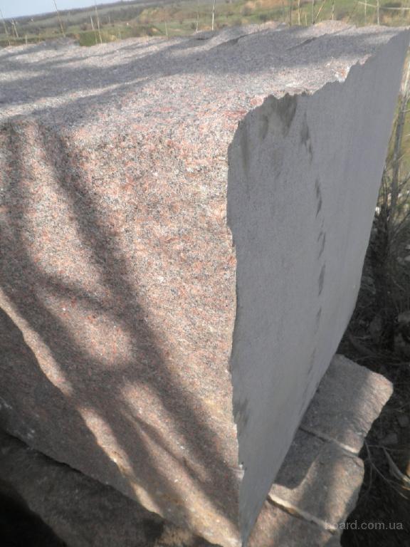 Ciężki, surowy blok różowego granitu o nierównych krawędziach, leżący na ziemi w plenerze. Widoczne ślady obróbki kamienia.