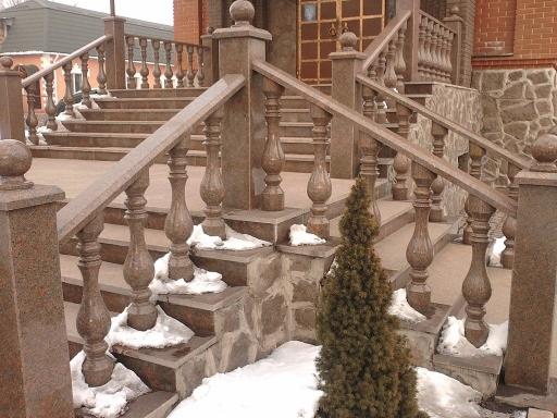 Granitowe schody zewnętrzne z balustradą w odcieniach brązu, z dekoracyjnymi tralkami i kulami na słupkach, częściowo pokryte śniegiem. Widoczny fragment elewacji budynku.