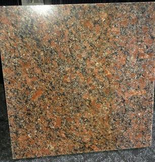 Błyszcząca, kwadratowa płyta z polerowanego granitu w odcieniach czerwieni i czerni, z widoczną ziarnistą strukturą, leżąca na szarej powierzchni.