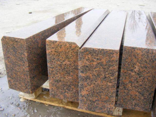 Polerowane, brązowo-czarne kostki granitowe z fazowanymi krawędziami, ułożone na palecie. Widoczne odbicia światła na powierzchni kamienia.