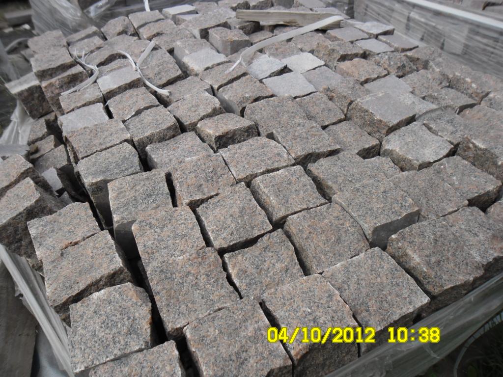 Szare kostki granitowe ułożone w regularny wzór, widoczne białe sznurki i data w prawym dolnym rogu. Kostka o szorstkiej fakturze, przygotowana do transportu.