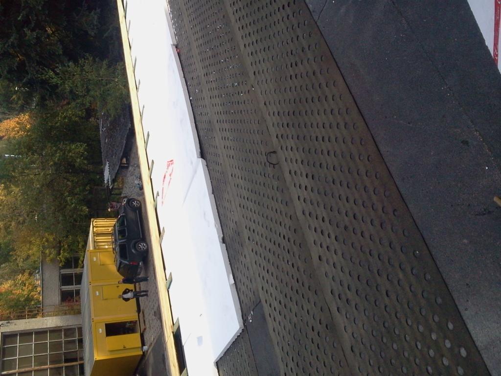 Dach z papy z perforacją i białą izolacją termiczną w trakcie montażu, widok z góry na budynek i samochód. Etap prac dekarskich.