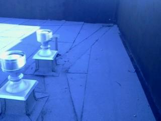 Fragment dachu z kominkami wentylacyjnymi. Widoczne łączenia papy i niewielkie uszkodzenia. Ujęcie z góry, oświetlenie naturalne.