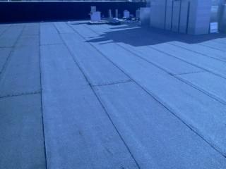 Szczegółowe ujęcie płaskiego dachu pokrytego papą termozgrzewalną, z widocznymi łączeniami i fakturą materiału. W tle jasne bloczki betonu komórkowego.