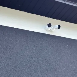 Dwie kamery monitoringu Hikvision zamontowane na białej ścianie budynku z szarą elewacją i czarnym okapem.