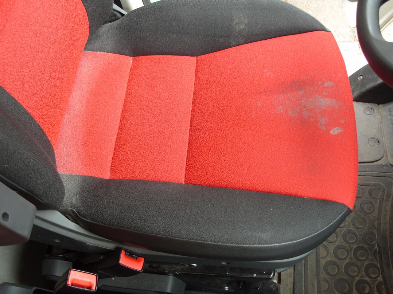 Czerwono-czarne, tekstylne siedzenie samochodowe z widocznymi plamami na czerwonej powierzchni, sugerujące potrzebę prania tapicerki.