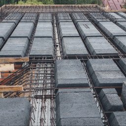 F.H.U. Ciapka Rafał Usługi Budowlane - Strop żebrowy Teriva w trakcie montażu: betonowe pustaki ułożone między żebrami, zbrojenie stalowe, drewniane podpory. Widok z góry na budowę stropu.