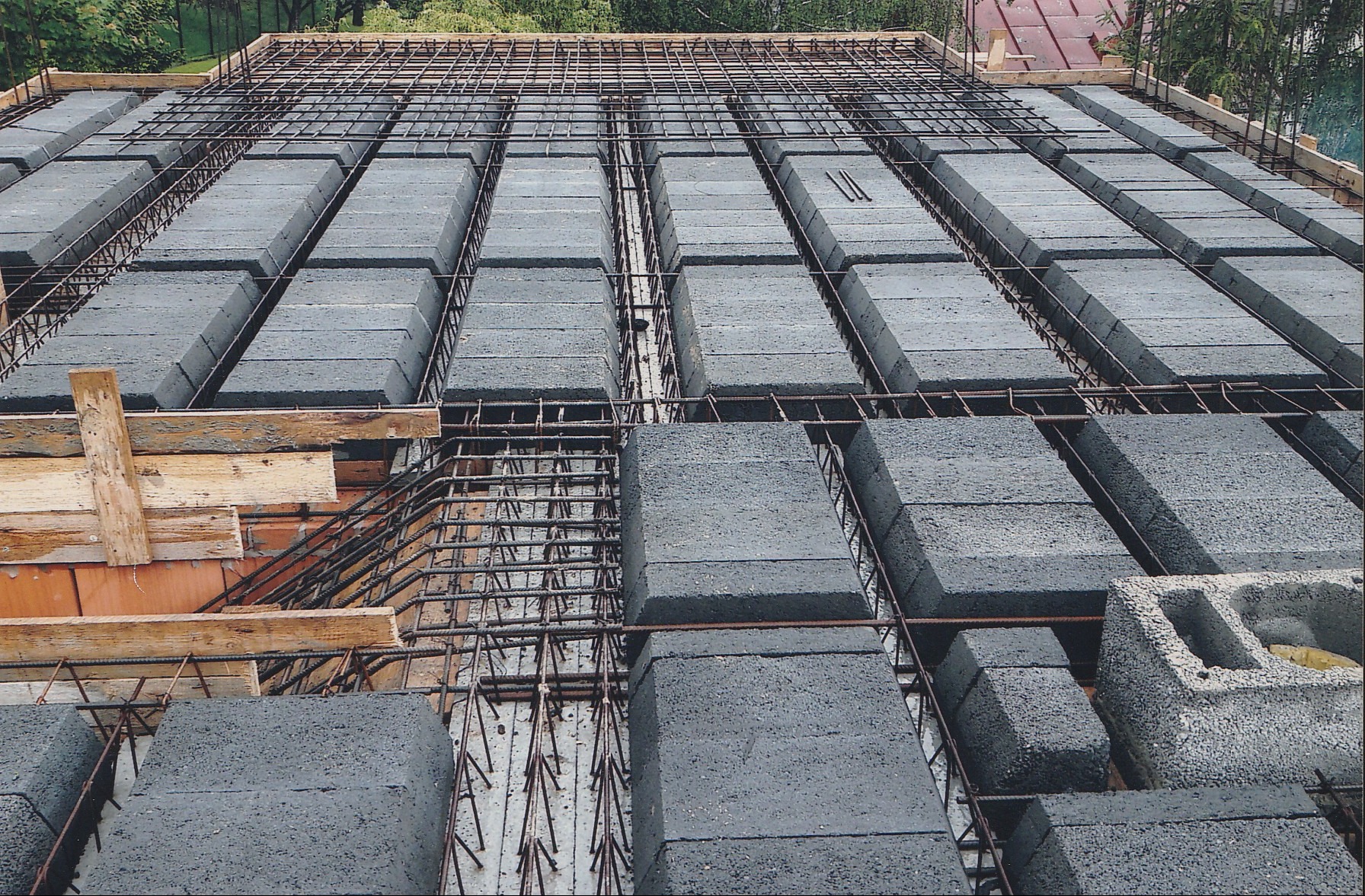 Strop żebrowy Teriva w trakcie montażu: betonowe pustaki ułożone między żebrami, zbrojenie stalowe, drewniane podpory. Widok z góry na budowę stropu.