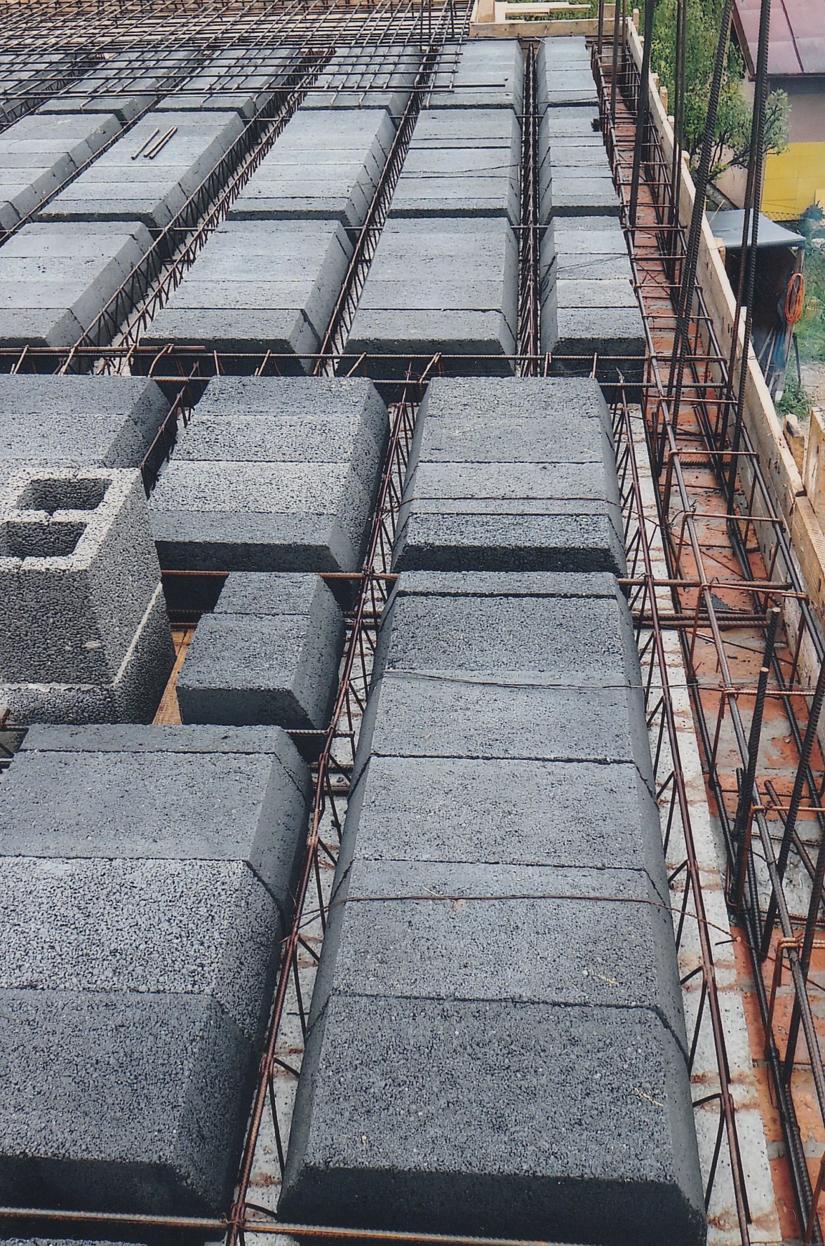 Strop żebrowy z szalunkiem i zbrojeniem, widok z góry. Szare bloczki ułożone w rzędach, pomiędzy nimi zbrojenie. Widoczne elementy drewnianego szalunku.