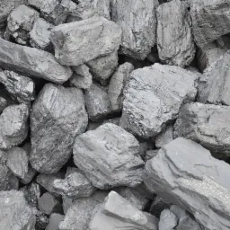 Stos szarego węgla kamiennego o nieregularnych kształtach i wyraźnej strukturze, z widocznymi refleksami światła na niektórych bryłach.
