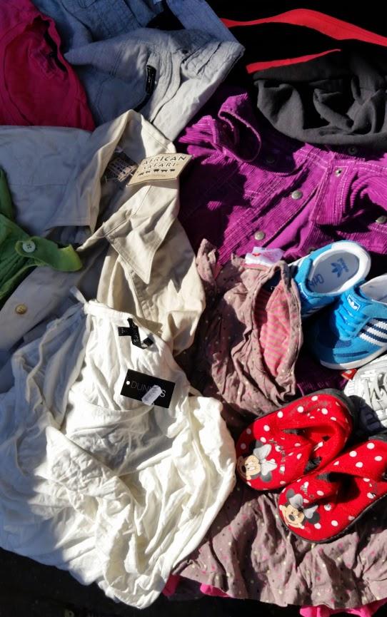 Stos różnorodnych ubrań i butów dla dzieci i dorosłych, w tym koszule, spodnie, kurtka sztruksowa, trampki Adidas i czerwone kapcie w białe kropki z motywem Myszki Minnie.