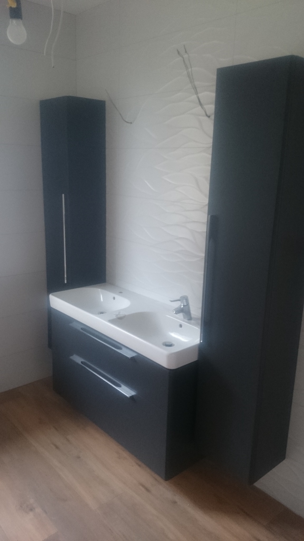 Nowoczesna łazienka z podwójną umywalką, szafkami w kolorze grafitowym i dekoracyjną białą ścianą z motywem fal.