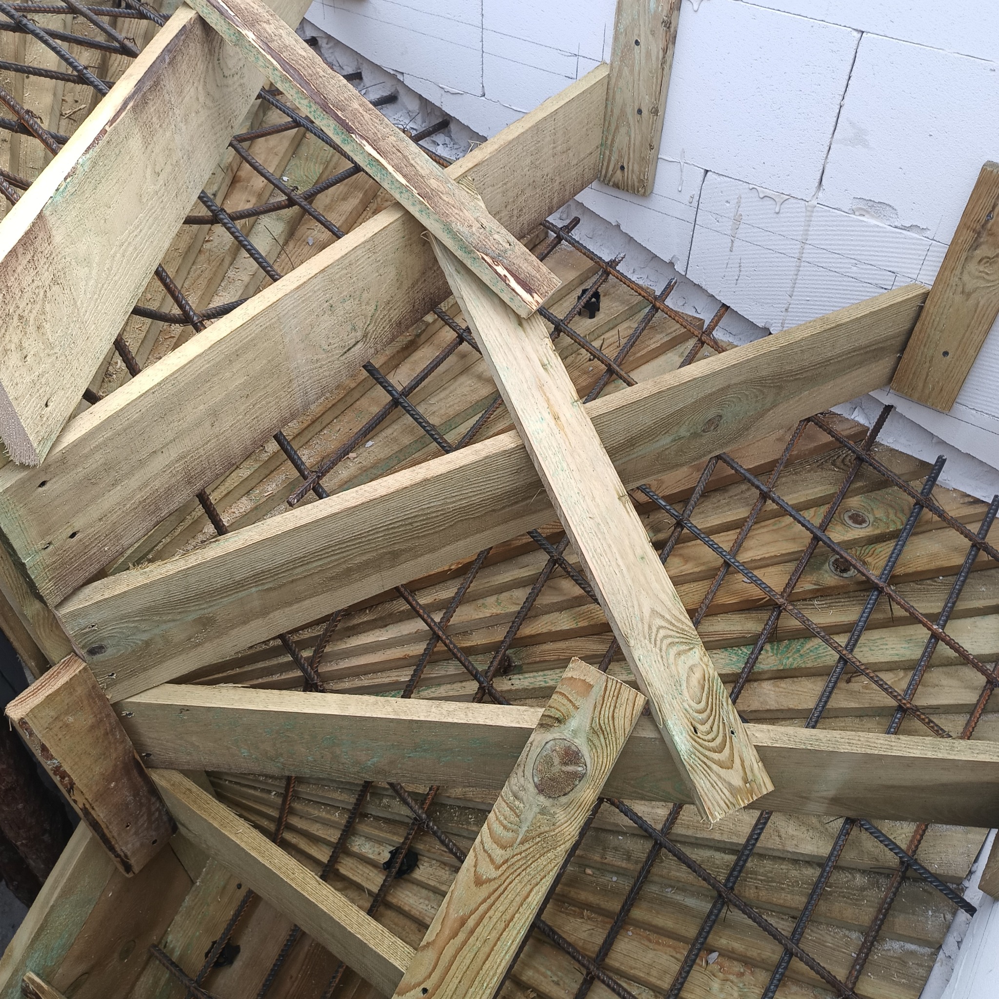 Zbrojenie i szalunek pod wylewkę stropu z betonu komórkowego. Widoczne drewniane deski, stalowe pręty i białe bloczki. Kątowe ujęcie z góry.