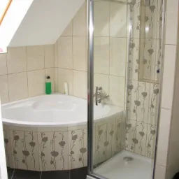 Narożna kabina prysznicowa z motywem kwiatowym i narożna wanna w łazience na poddaszu z oknem dachowym.