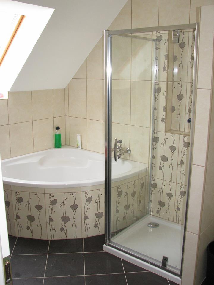 Narożna kabina prysznicowa z motywem kwiatowym i narożna wanna w łazience na poddaszu z oknem dachowym.