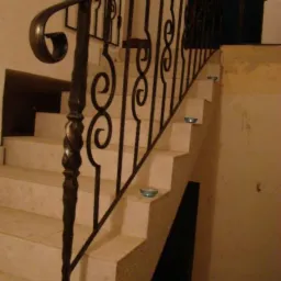 Kuta balustrada schodowa z ozdobnymi elementami w kształcie spirali, zamontowana na marmurowych schodach. Widoczne detale wykończenia i zdobienia.