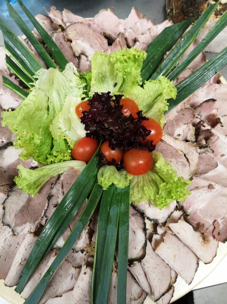 Dekoracyjnie ułożone plastry pieczonego mięsa z dodatkiem zielonej i czerwonej sałaty oraz pomidorków koktajlowych, tworzące kompozycję na przyjęcie.