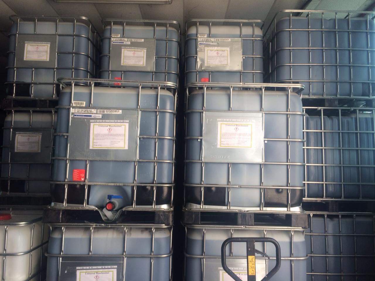 Stos palet z pojemnikami IBC wypełnionymi płynem, etykiety ostrzegawcze Universal Waschmittel widoczne na każdym pojemniku, ujęcie z bliska.