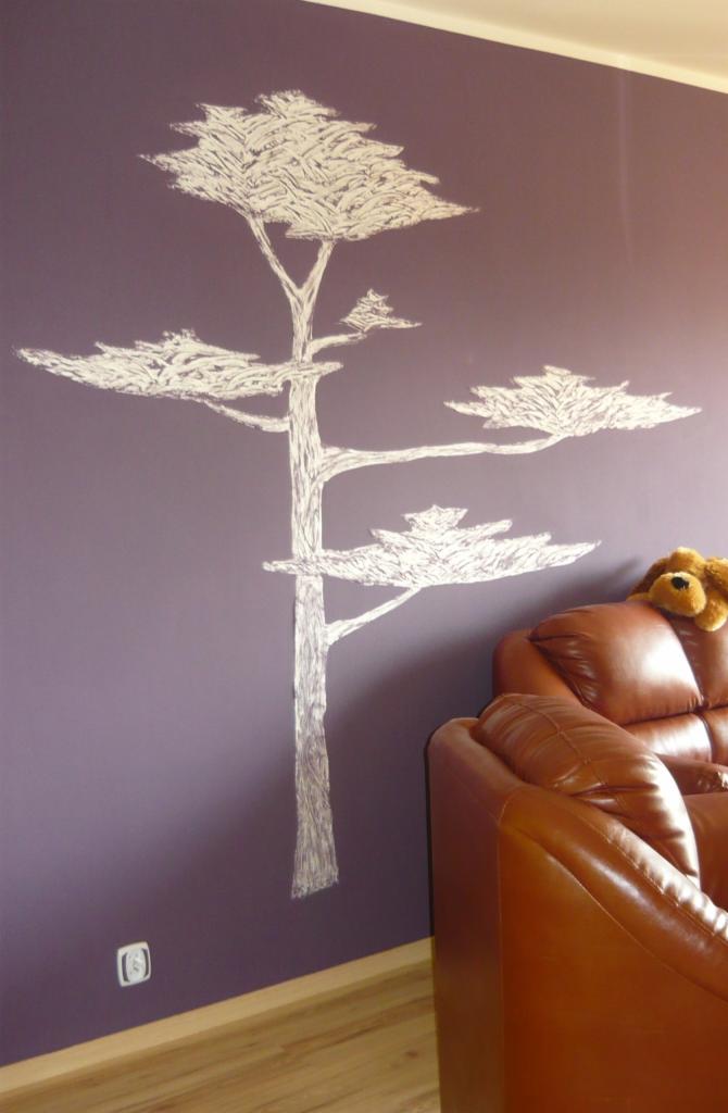 Ręcznie malowane, białe drzewo na fioletowej ścianie w salonie, obok skórzana kanapa. Dekoracja ściany w pokoju dziennym. Widoczny fragment podłogi.