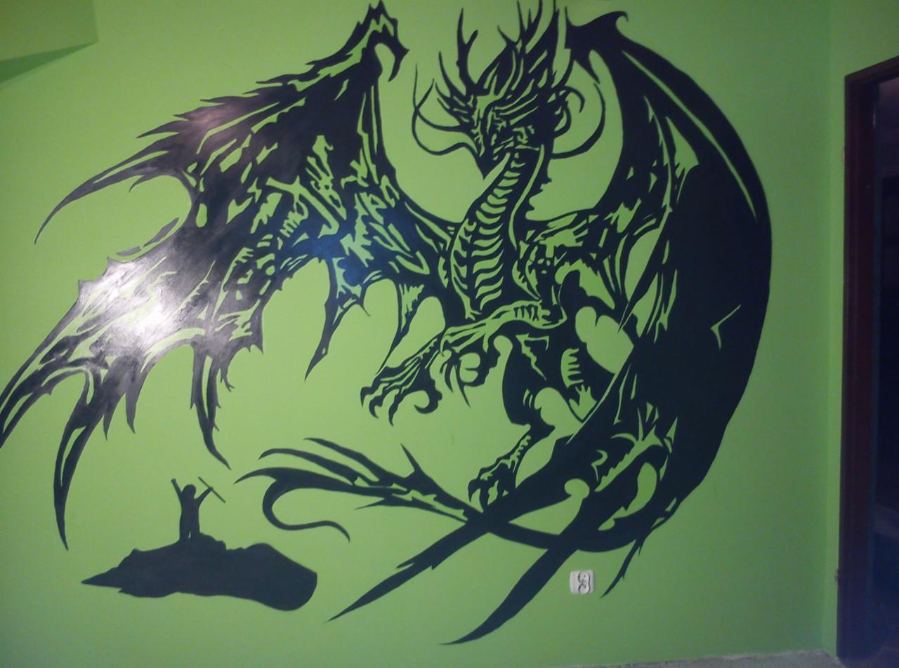 Zielona ściana z czarnym malunkiem smoka i małej postaci. Kąt ujęcia od dołu, widoczne gniazdko elektryczne przy podłodze, oraz fragment futryny drzwi.