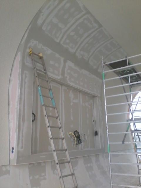 Szpachlowanie łukowego sufitu i ściany z oknem, widoczna drabina i rusztowanie, ściany przygotowane do dalszych prac wykończeniowych.