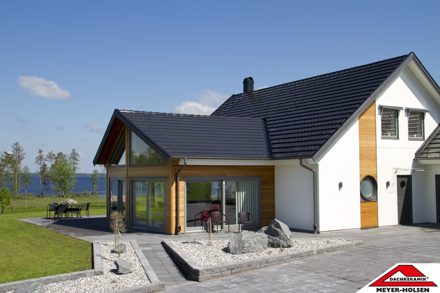 Nowoczesny dom jednorodzinny z ciemną dachówką ceramiczną, drewnianą elewacją i dużymi przeszkleniami w słoneczny dzień.