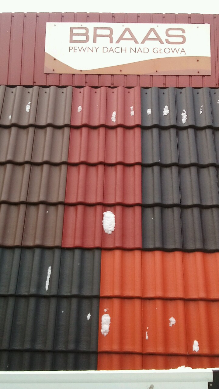 Ekspozycja dachówek ceramicznych w różnych kolorach (brązowy, czerwony, czarny, pomarańczowy) z logo producenta 'BRAAS' i sloganem 'PEWNY DACH NAD GŁOWĄ', na niektórych dachówkach leży śnieg.