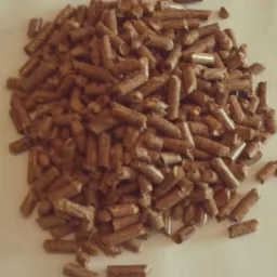 Kupa brązowego pelletu drzewnego na jasnym tle, widoczne pojedyncze granulki, oświetlenie naturalne, lekki cień. Struktura drewna wyraźnie widoczna.