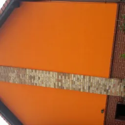 Pomarańczowa elewacja domu z ceglanym pasem dekoracyjnym i fragmentem ogrodu z kulistymi lampami.