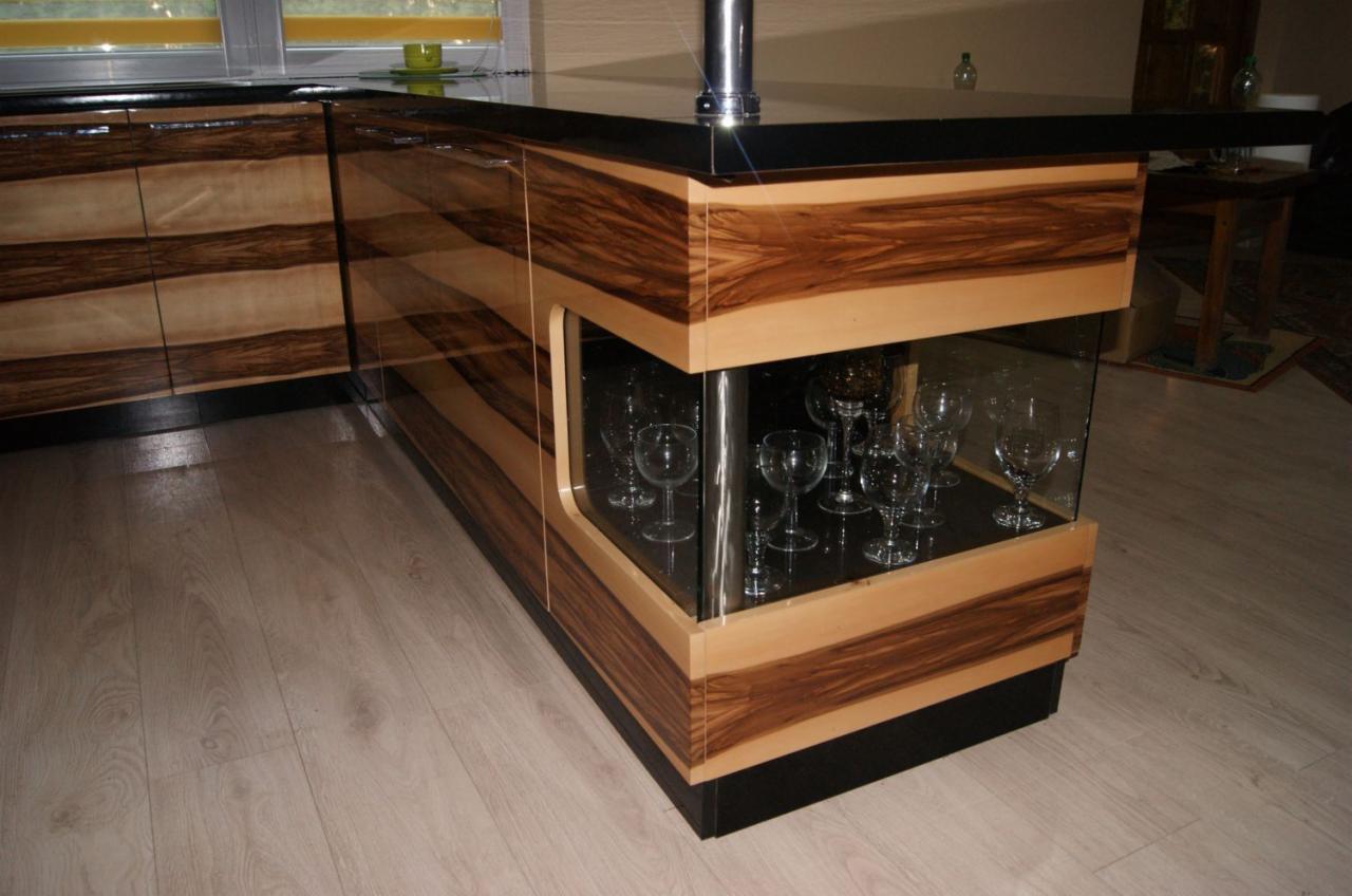 Nowoczesna wyspa kuchenna z egzotycznego drewna i szklaną witryną na kieliszki, czarny blat, oświetlenie okienne w tle.