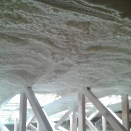 Ocieplenie poddasza pianką PUR widoczne między drewnianymi elementami konstrukcji dachu, nier&oacute;wnomierna struktura piany.