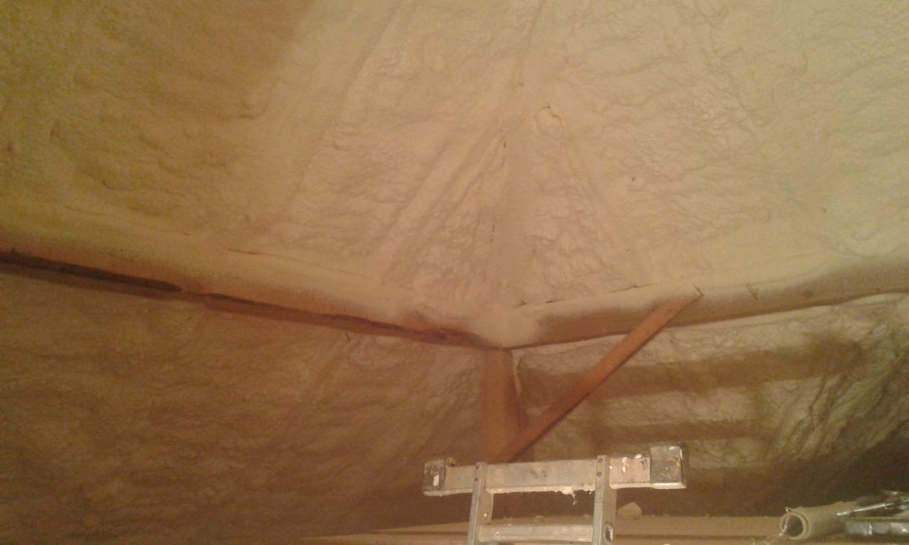 Poddasze po natrysku izolacji, widoczne drewniane elementy konstrukcyjne i drabina na pierwszym planie.