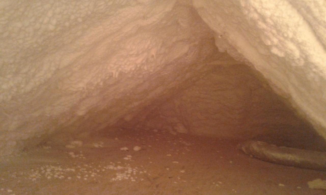 Strych po natrysku izolacji, widoczne nierównomierne pokrycie pianą i drobne białe odpryski na podłodze.