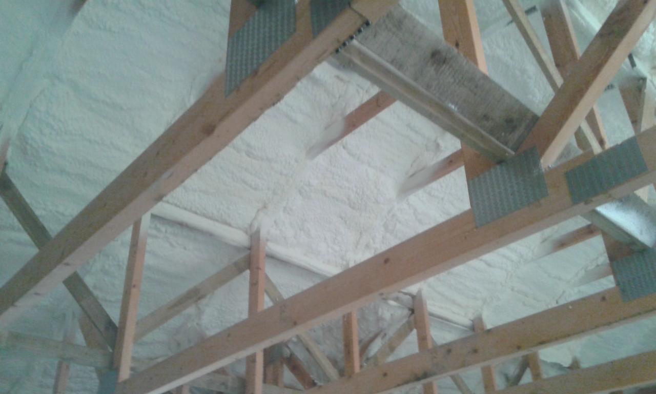 Poddasze z drewnianą konstrukcją dachu po ociepleniu pianką PUR, widoczne metalowe wzmocnienia belek.