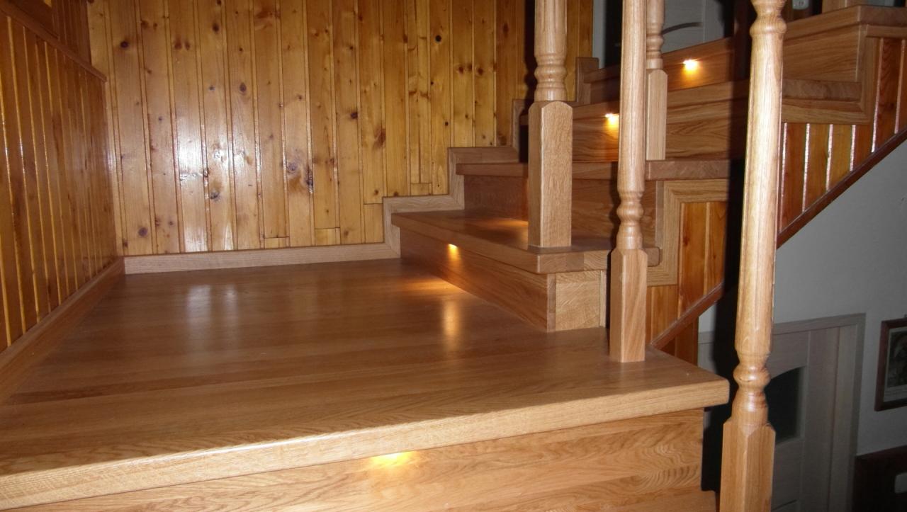 Drewniane schody z oświetleniem LED pod stopniami i boazerią na ścianie, widok z dołu.