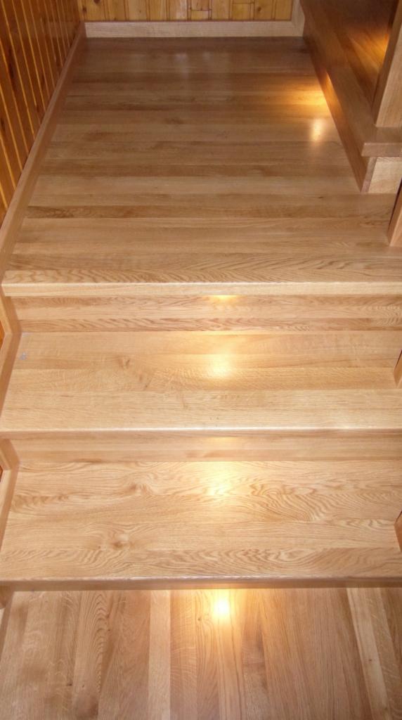 Jasne, dębowe stopnie schodów wewnętrznych z podświetleniem punktowym od spodu, widok z góry.