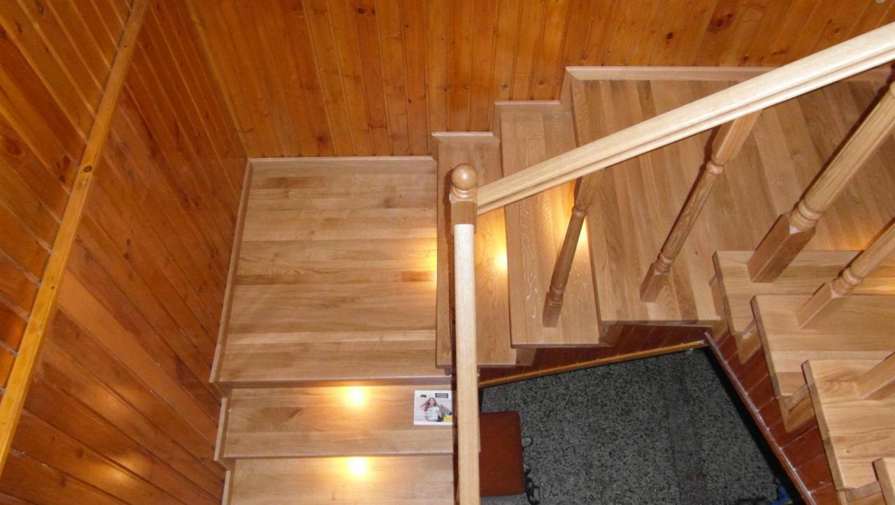 Widok z góry na jasne, drewniane schody z balustradą z okrągłymi zakończeniami, dopasowane do drewnianej boazerii na ścianach i suficie, mała naklejka na jednym ze stopni.