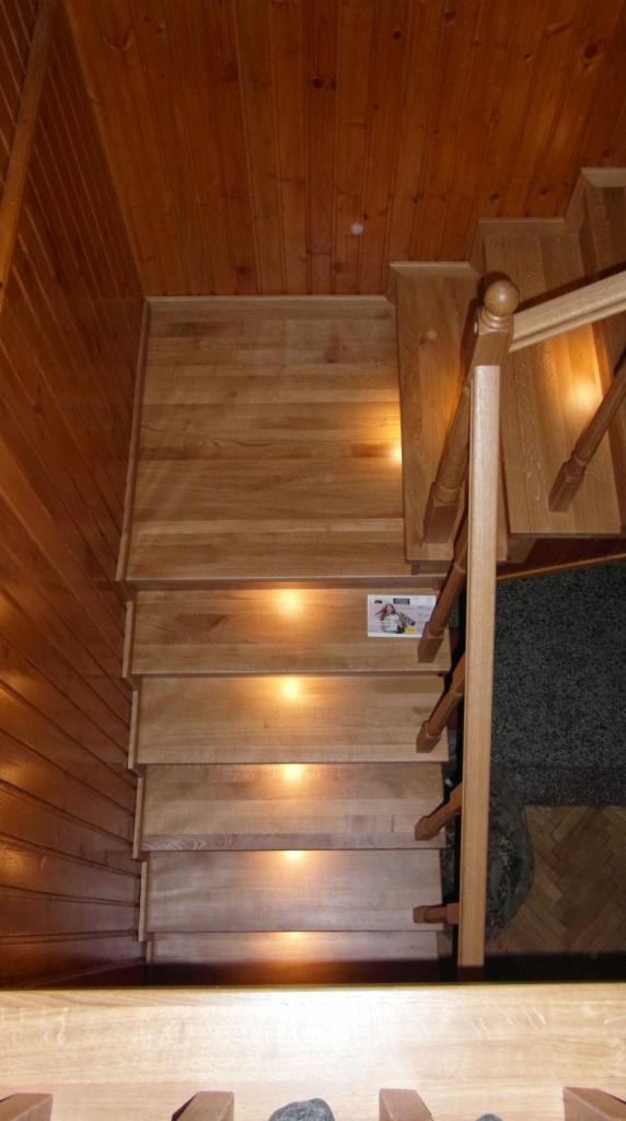 Wnętrze domu z drewnianymi schodami z podświetleniem LED i drewnianą boazerią na ścianach oraz drewnianą balustradą, widok z góry.