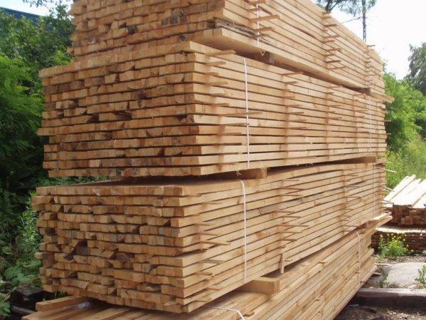 Stosy świeżo przetartego drewna w Kraków, zabezpieczone sznurkiem, czekają na transport. Widoczne słoje i naturalny kolor drewna na tle zieleni.