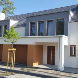 Nowoczesny segment bliźniaka z brązowymi drzwiami wejściowymi i bramą garażową, widok z niskiej perspektywy z elementami zagospodarowania terenu.